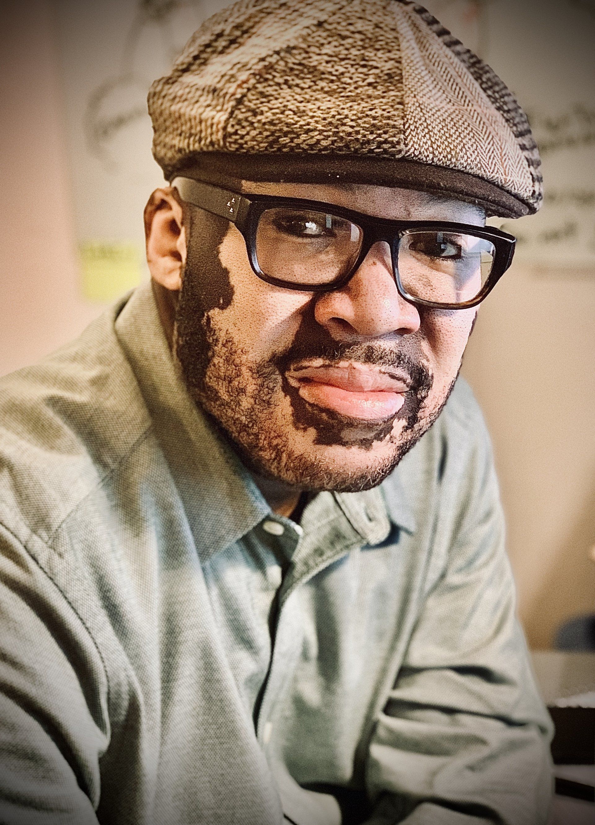 A man wearing glasses and a hat is smiling for the camera.