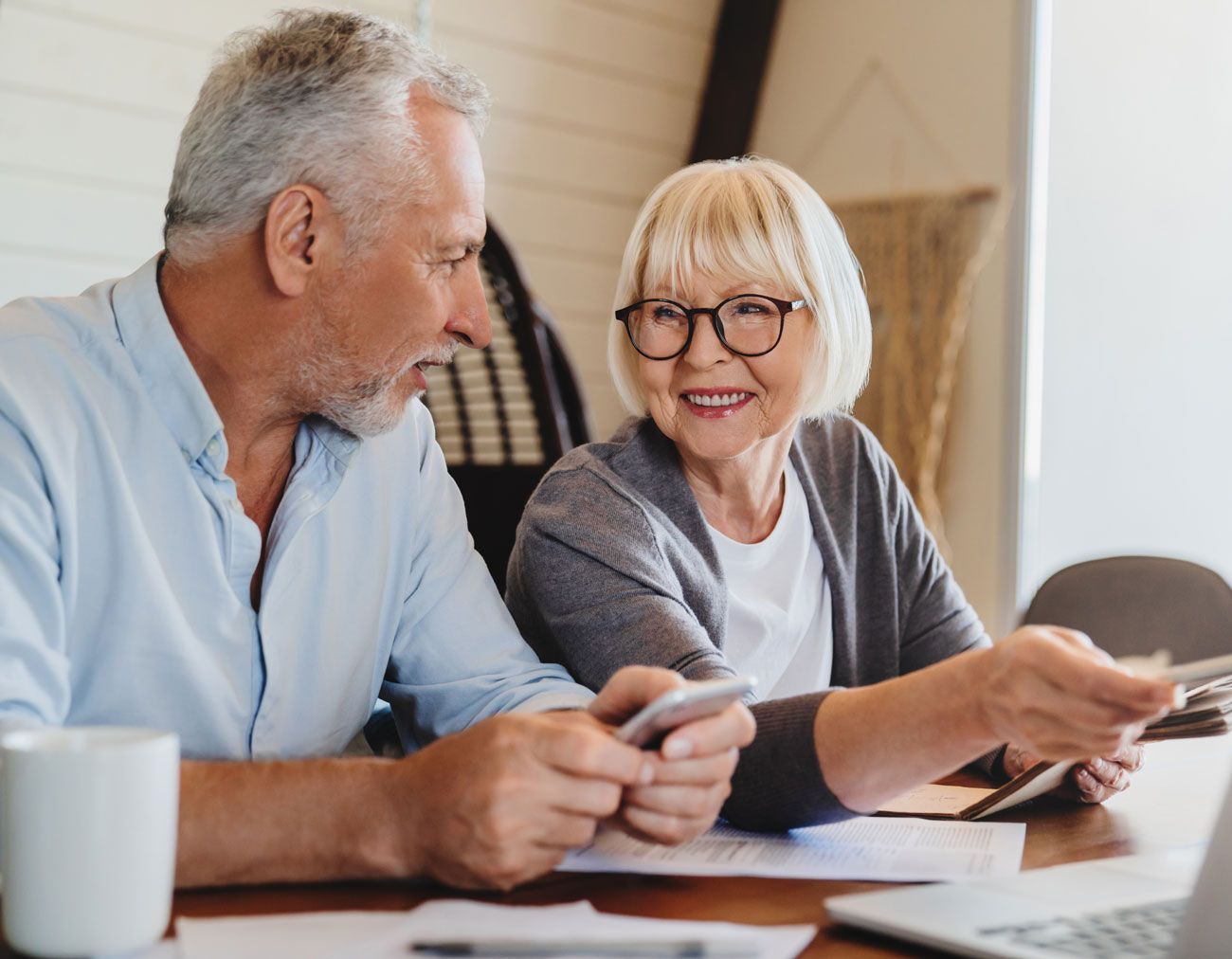 Older couple reviewing finances together at a table with a laptop, documents, and a smartphone.