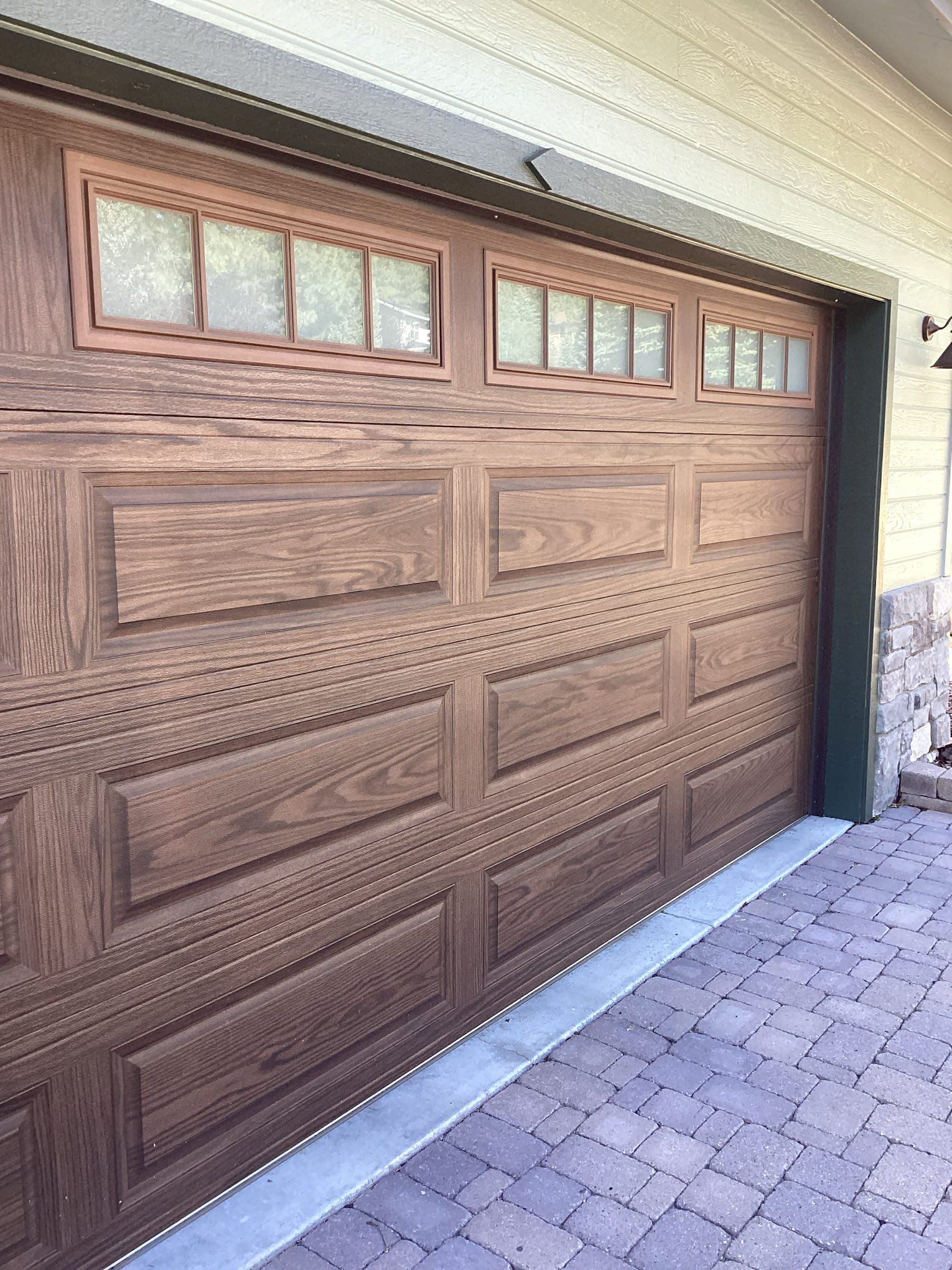A wooden garage door with a brick driveway in front of it.