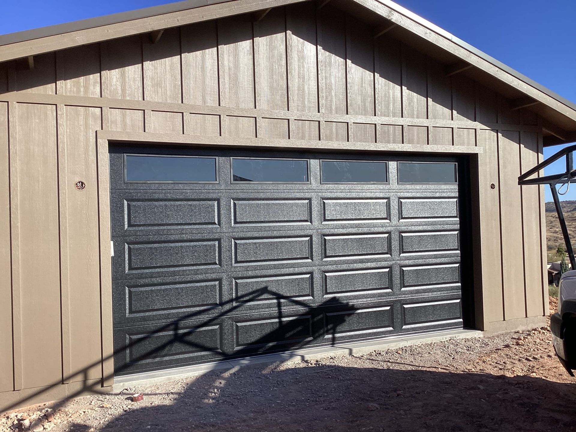 A brown garage with a black garage door and a car parked in front of it.