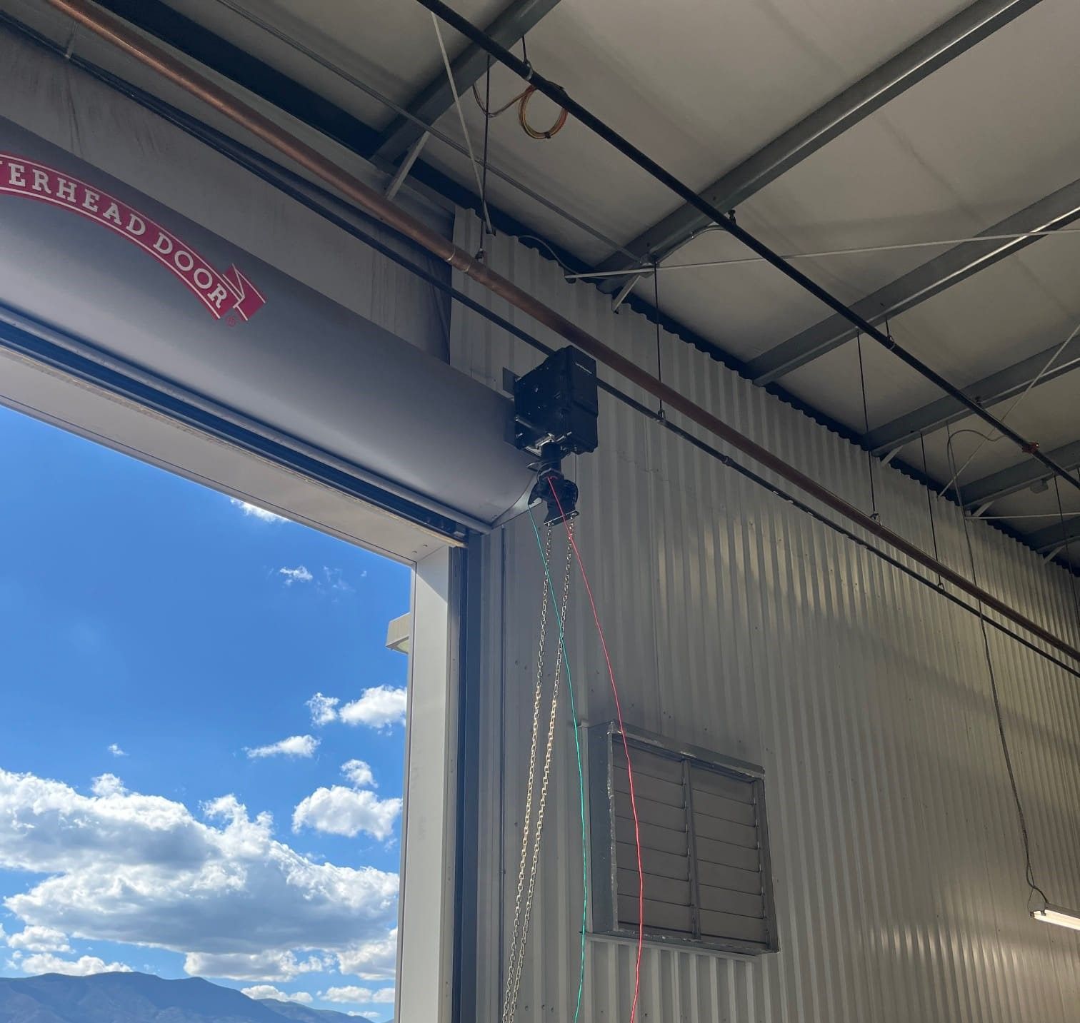Open industrial garage door, view of the sky. Overhead door mechanism visible.