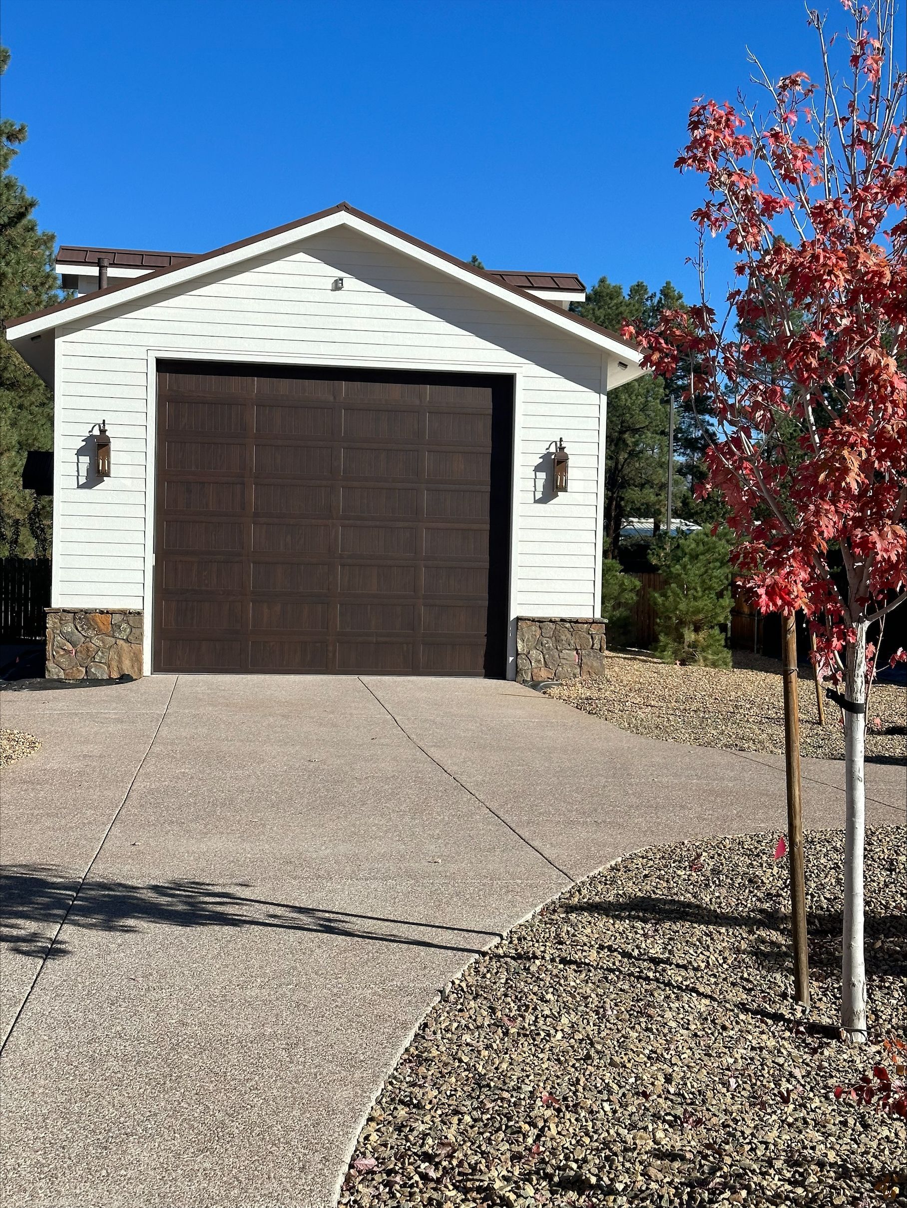 A white garage with a brown door and a tree in front of it