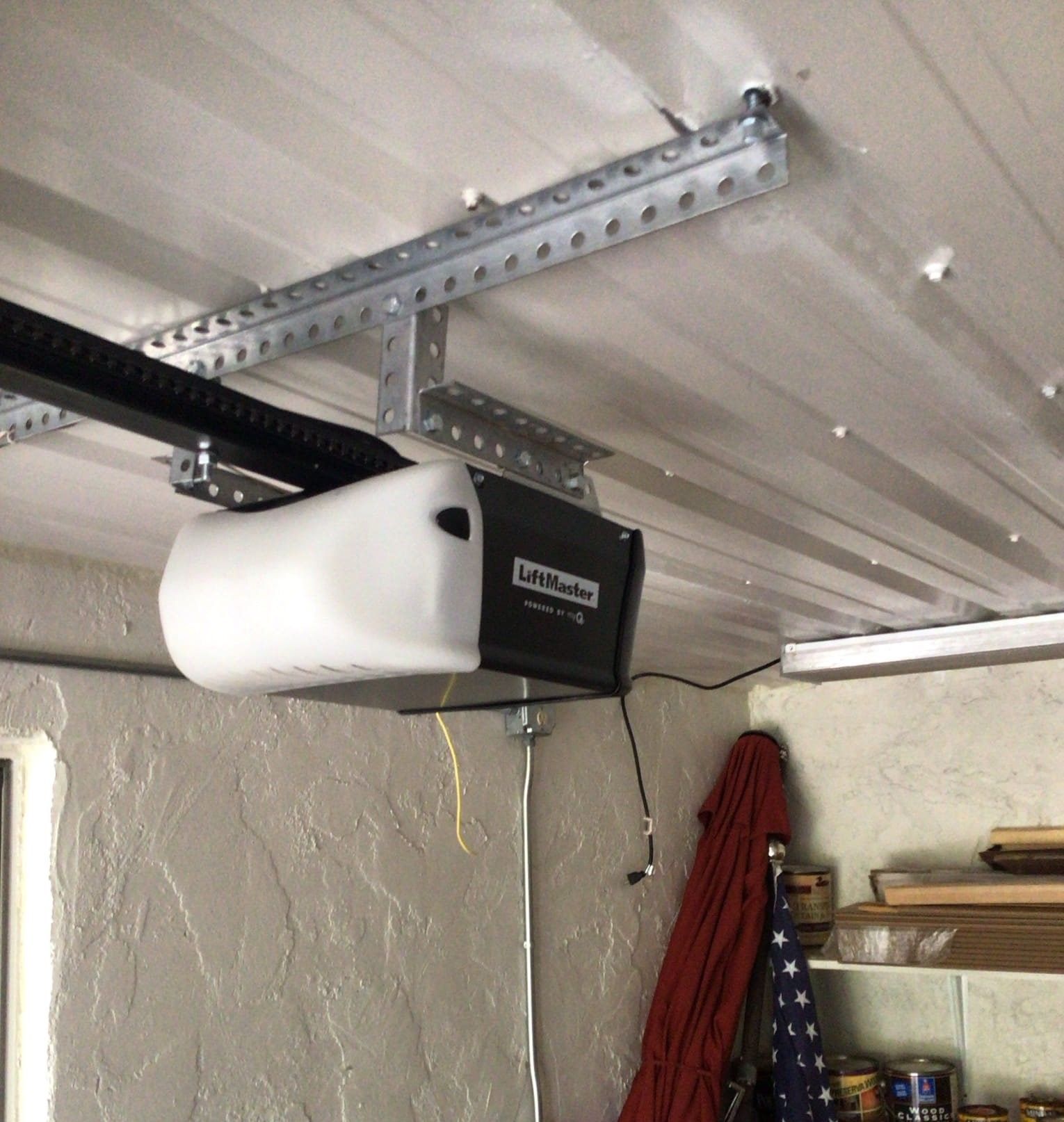 Garage door opener mounted on ceiling; white motor housing, black track and supporting hardware.