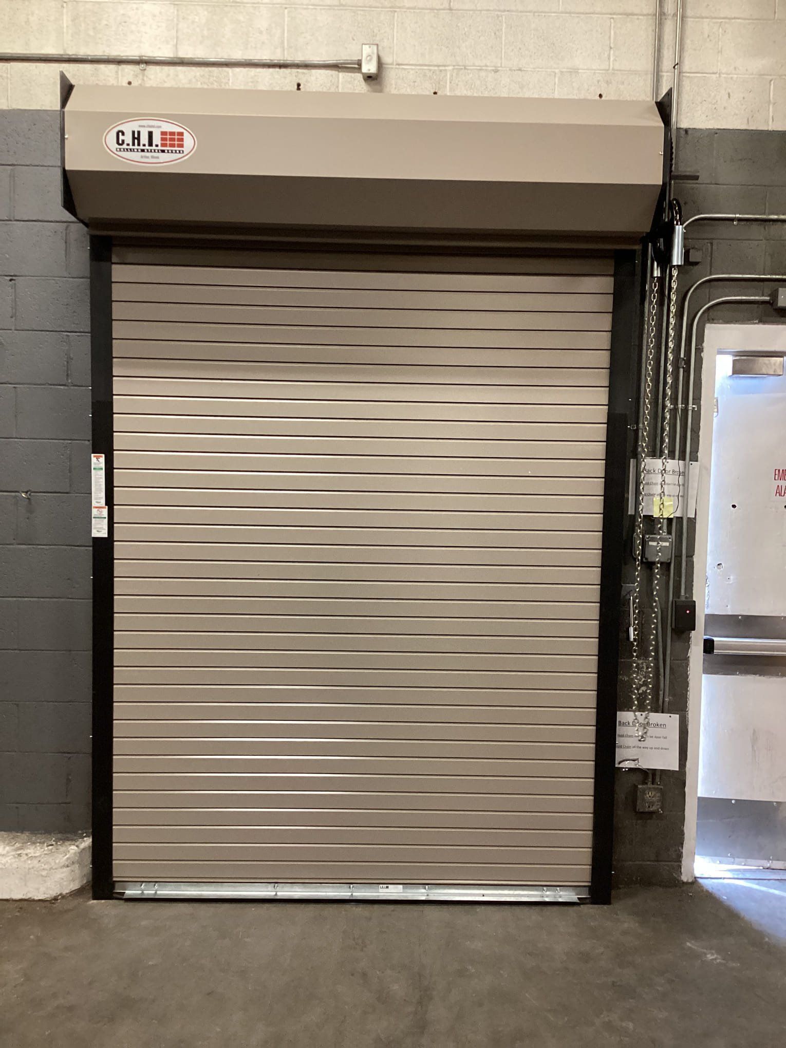 A roll up door is sitting in a warehouse next to a door.