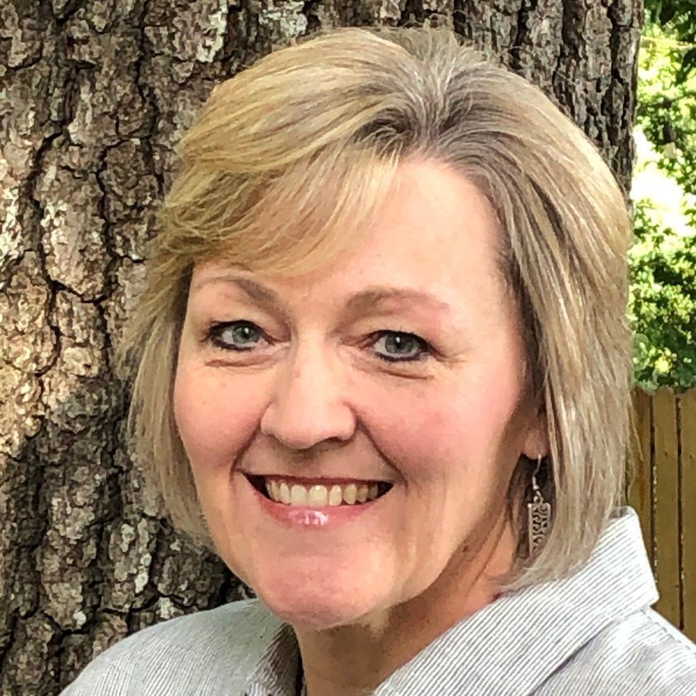 A woman is smiling in front of a tree.