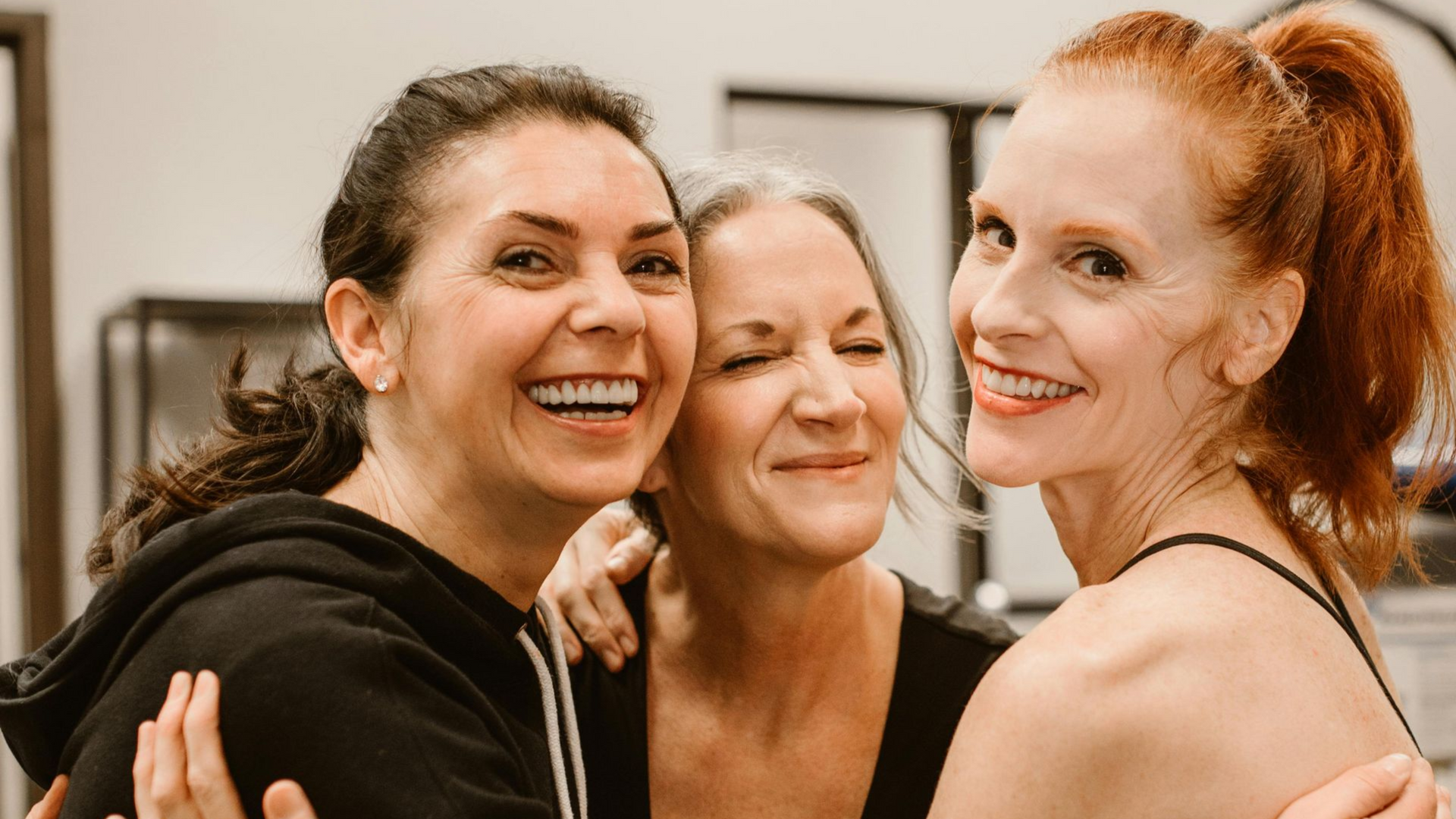 Man in gray shirt meditates on a mat outdoors, hands together, fountain in background.