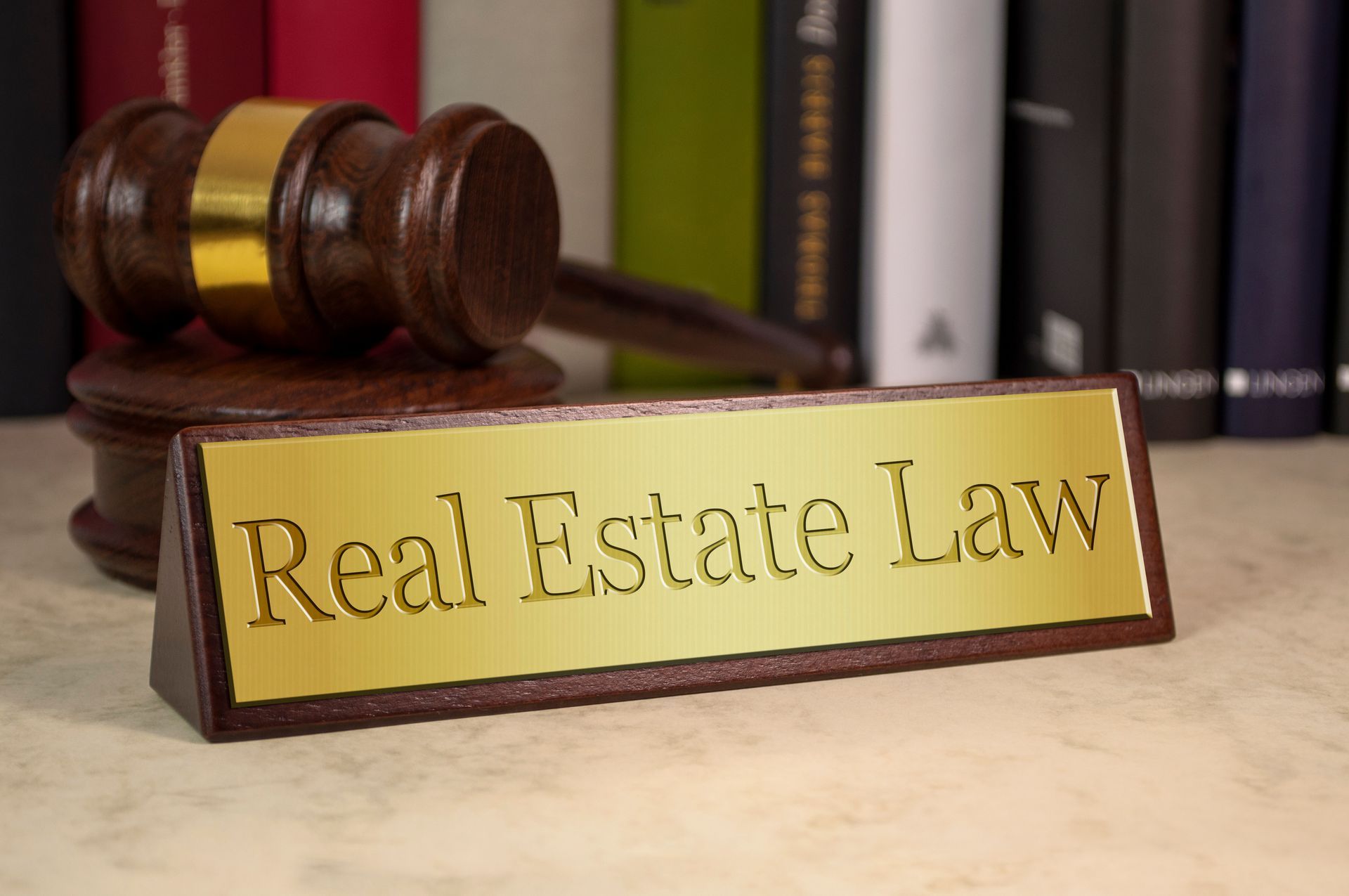 A wooden gavel beside a sign reading Real Estate Law on a desk with legal books behind.