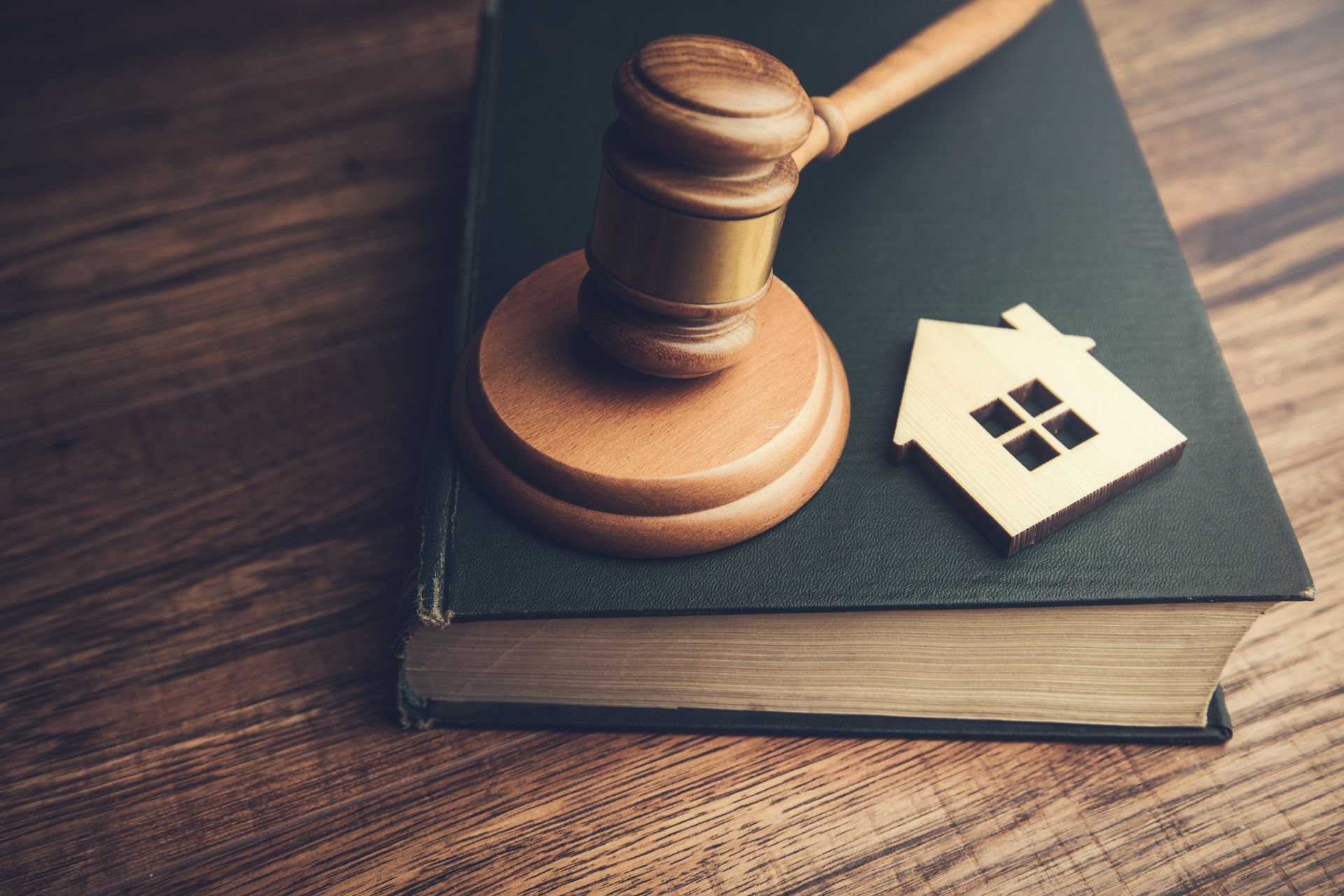 A wooden gavel and small house icon resting on a thick law book on a wooden desk.