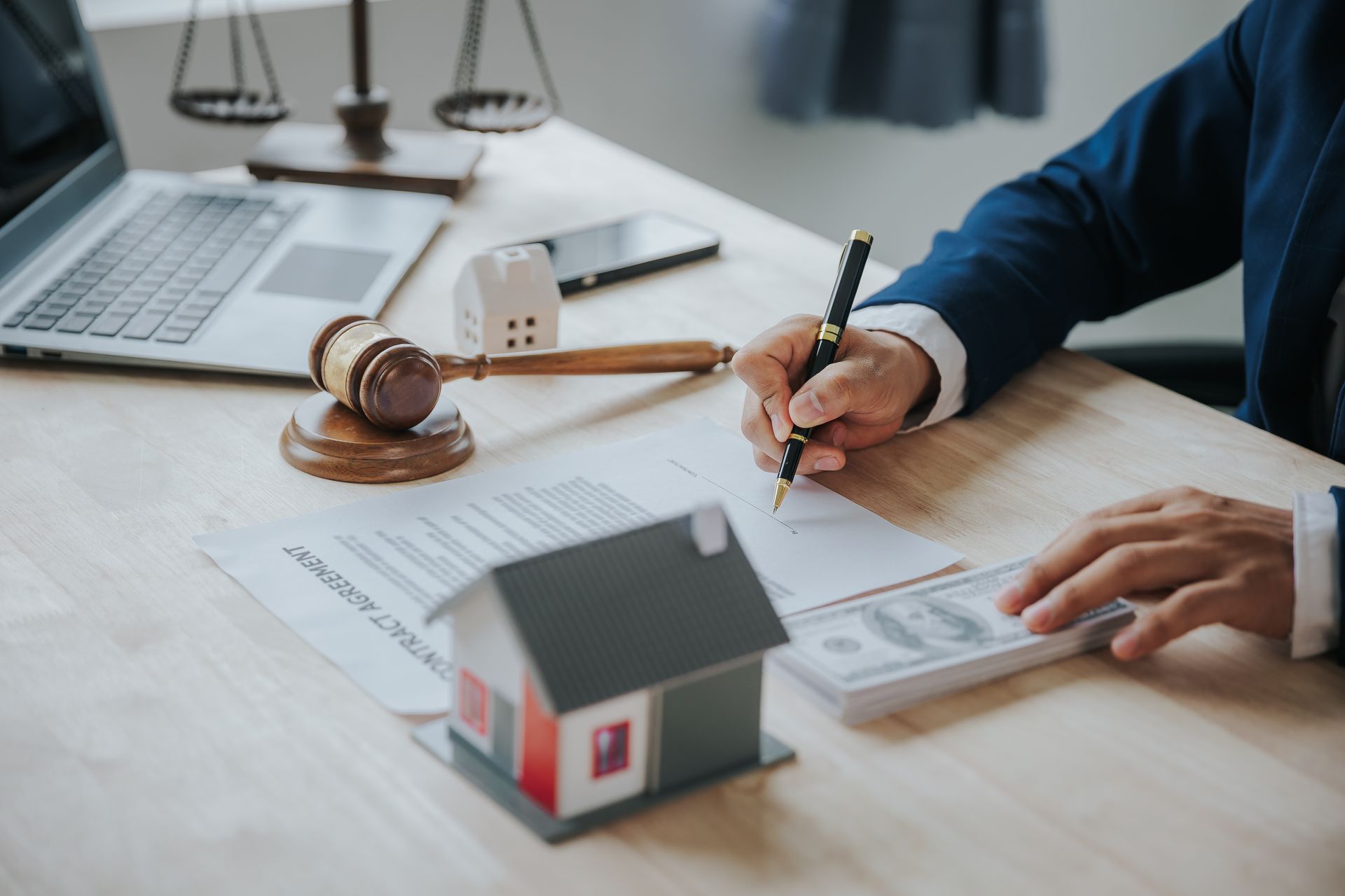 Real estate attorney handling property documents at office desk with miniature house and gavel.