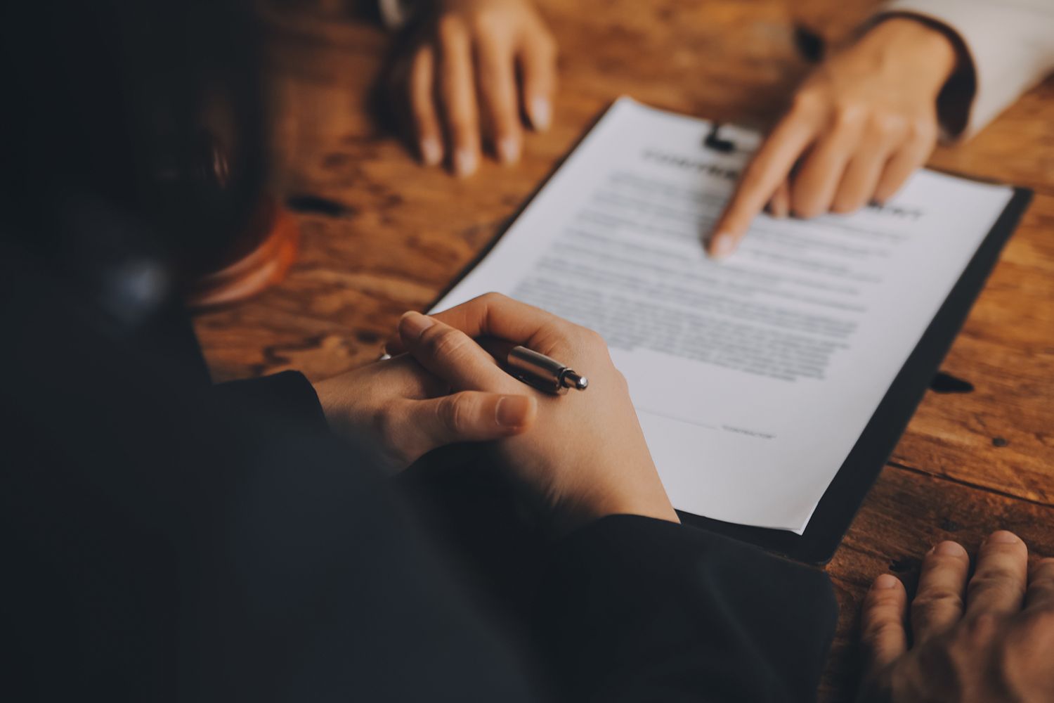 A close-up of a lawyer counseling a client on signing a document on a table.