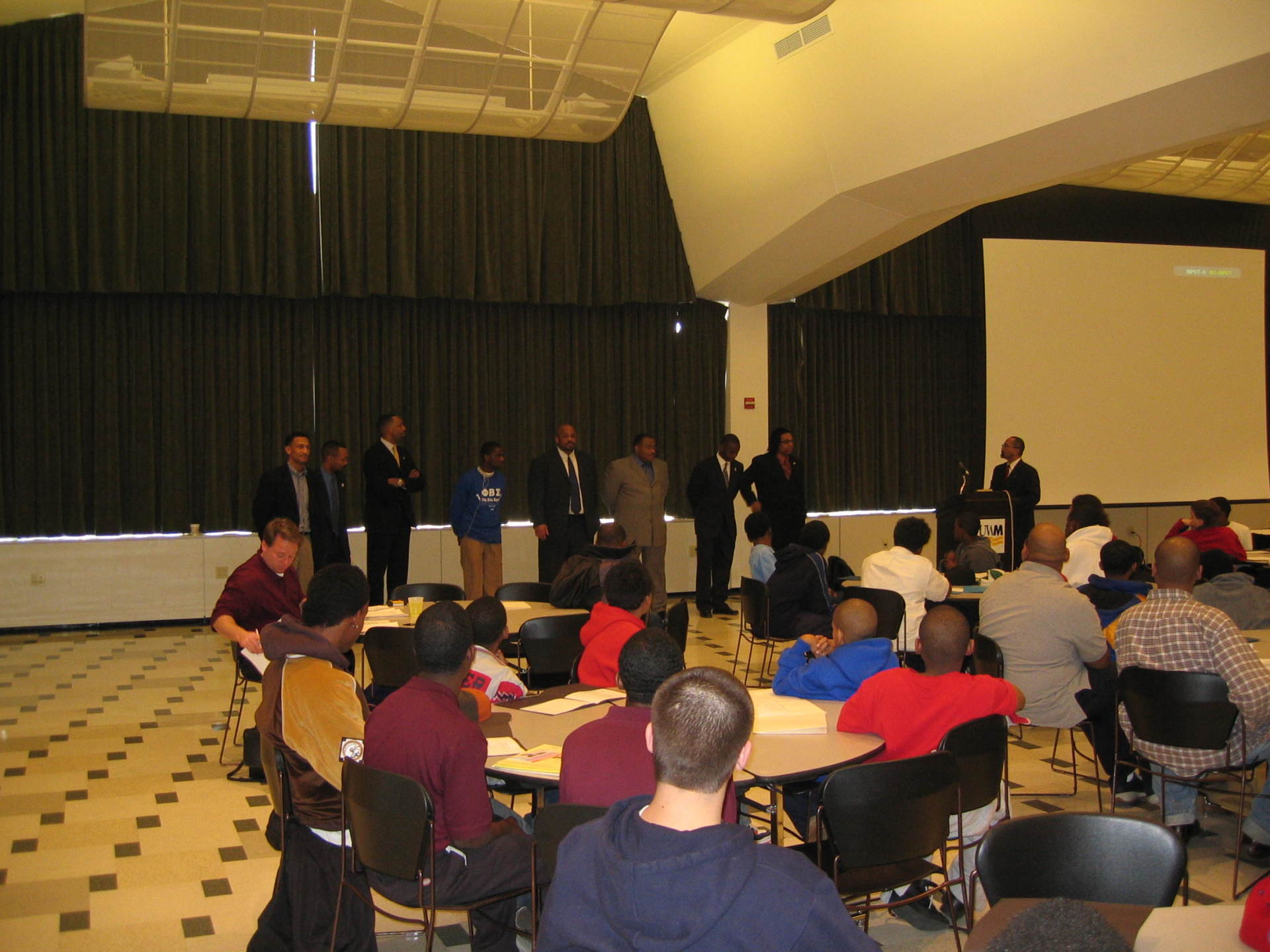 Panel of male and female speakers  standing in front of room filled with students at previous Positive Images Leadership Teen Summit meeting in Milwaukee