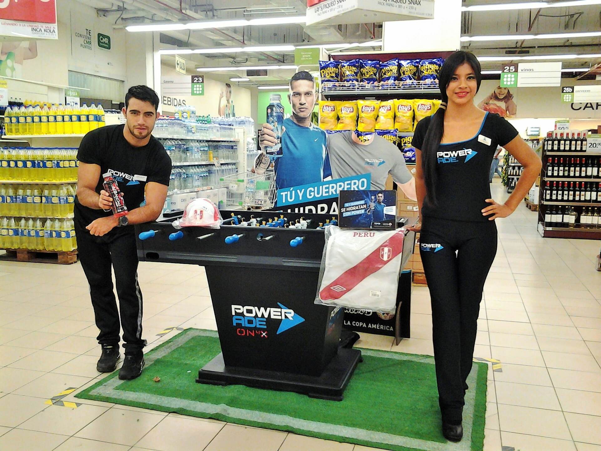 Dos hombres y una mujer de pie frente a un expositor de bebidas energéticas.
