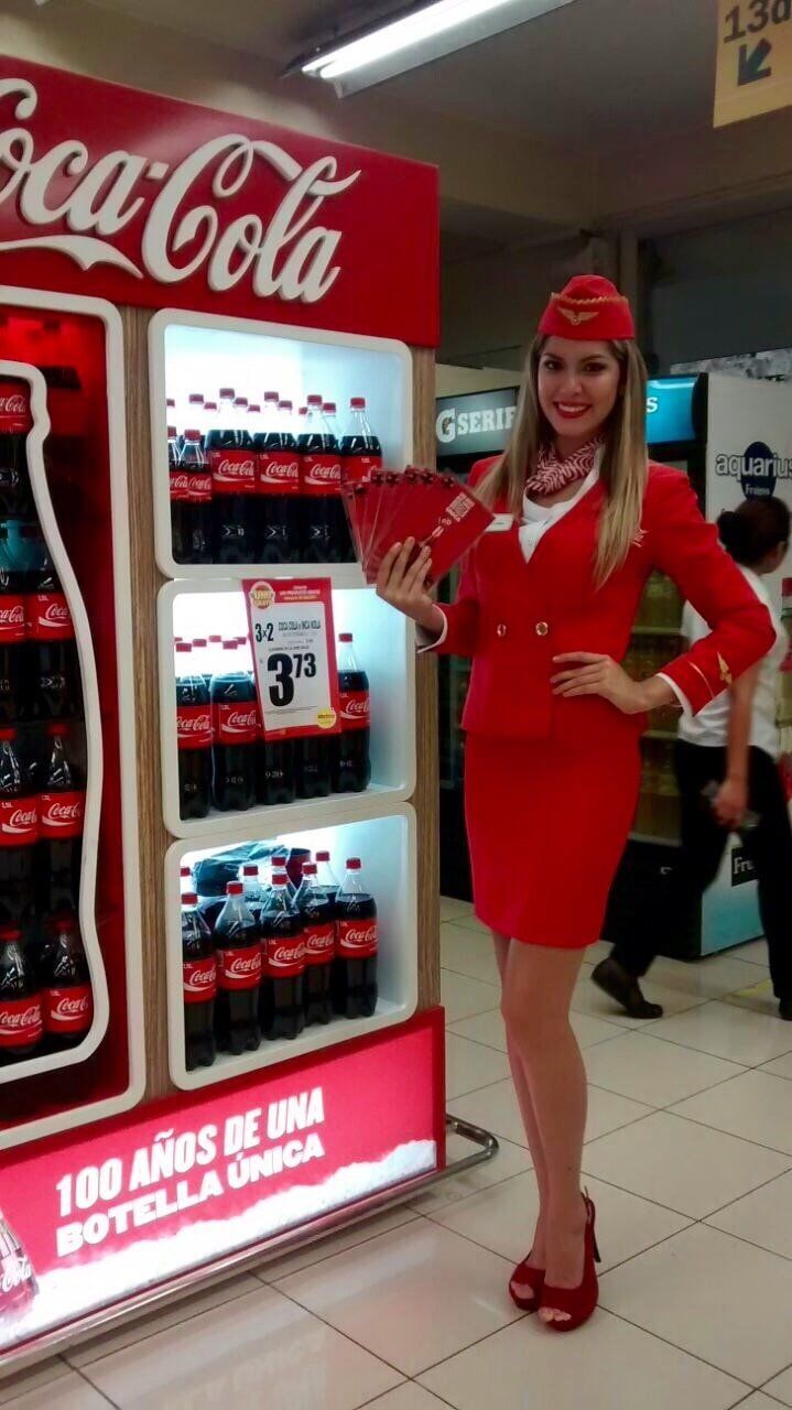 Una mujer con un vestido rojo está parada frente a un expositor de Coca Cola.