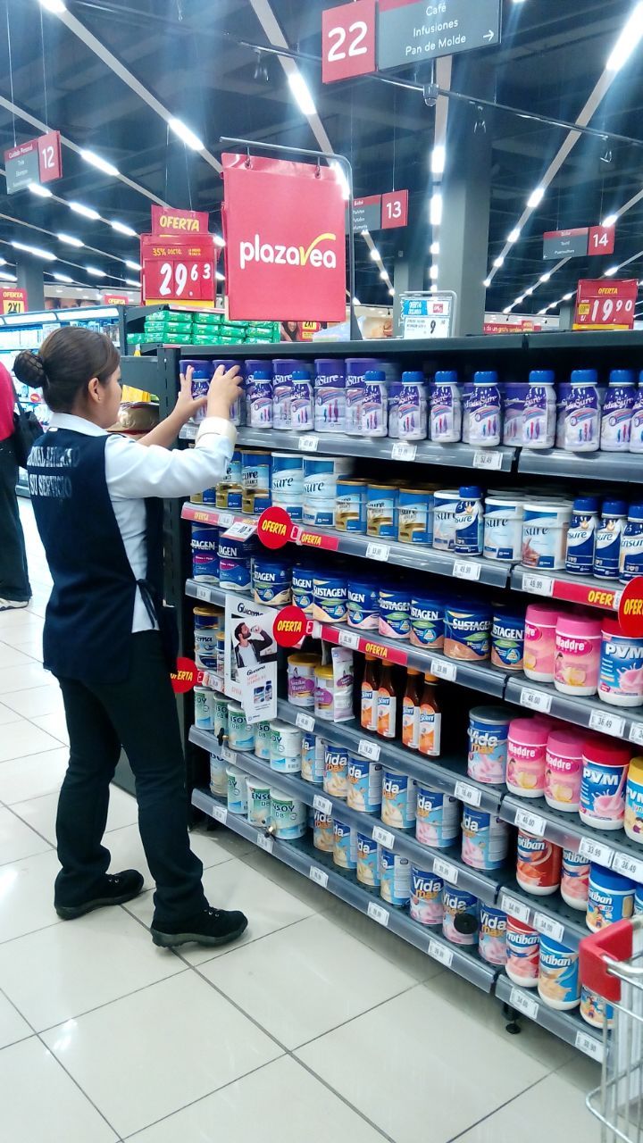 Una mujer está trabajando en un estante en una tienda de comestibles.