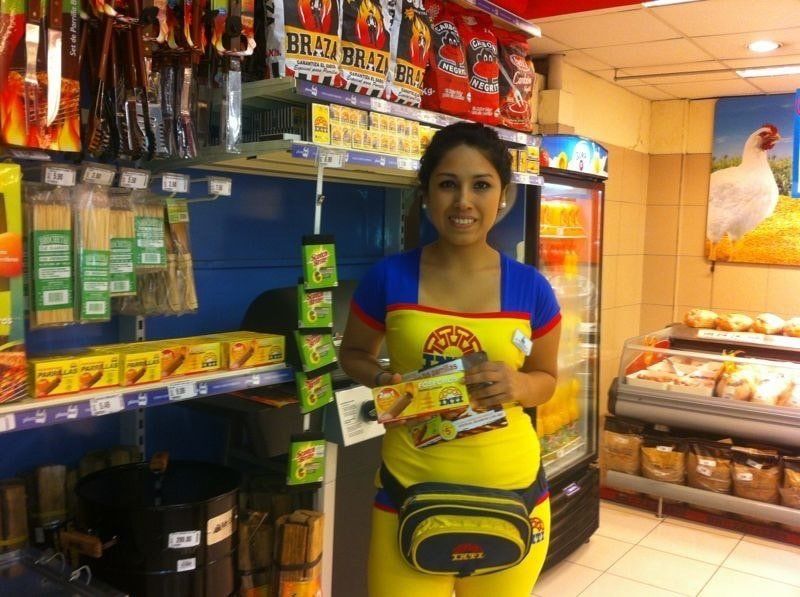 Una mujer con un delantal amarillo está parada en una tienda de comestibles.
