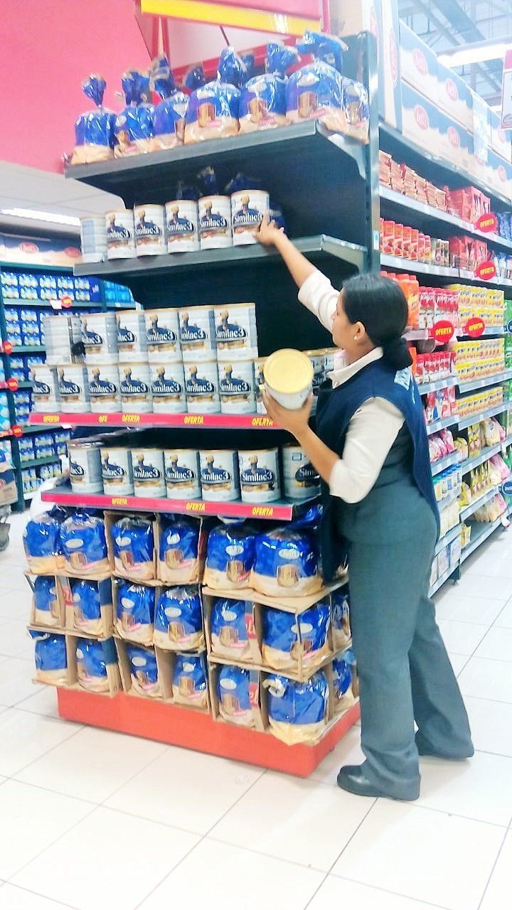 Una mujer está parada en una tienda de comestibles tratando de alcanzar algo en un estante.