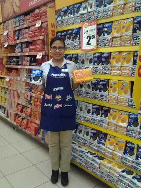 Una mujer con un delantal azul sostiene una caja de galletas Oreo.