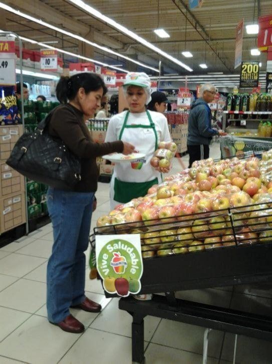 Una mujer está parada frente a una exhibición de manzanas en una tienda de comestibles.