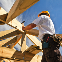 A man wearing a hard hat is working on a wooden structure