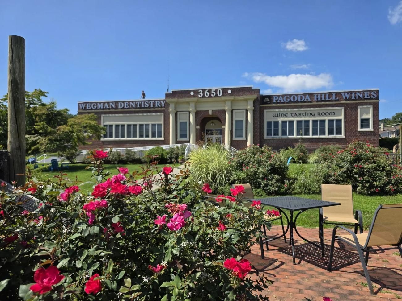 Pagoda Hill Wines building with roses and patio seating under blue sky.