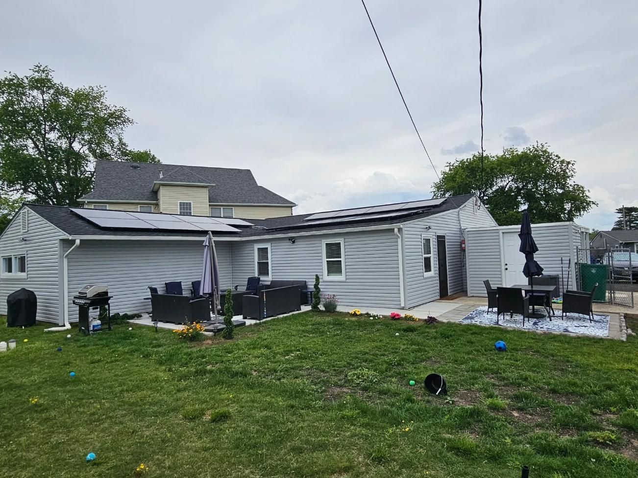 Backyard with house and solar panels on roof, patio furniture, green grass, and overcast sky.