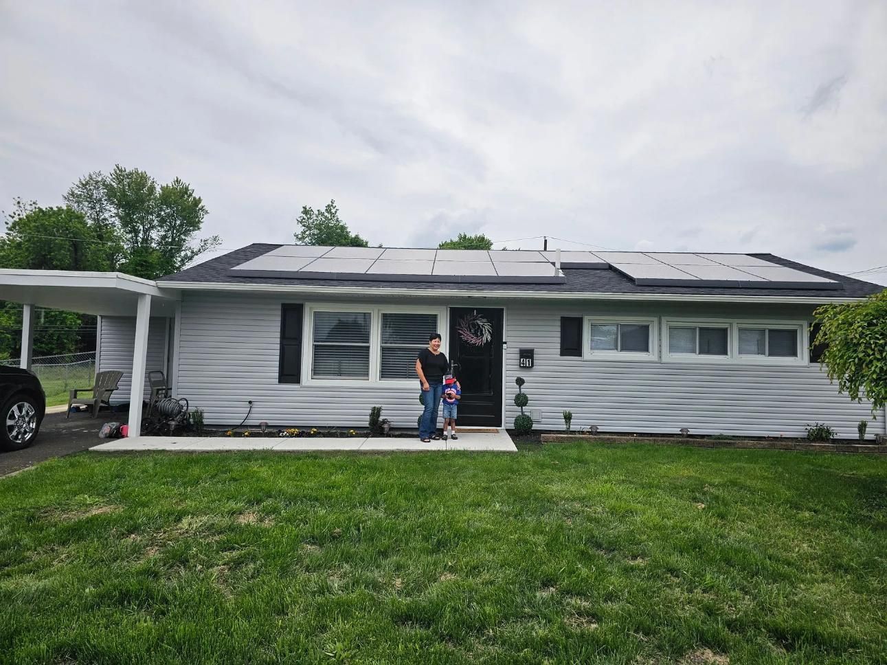 A person and a child stand in front of a house with solar panels on the roof.