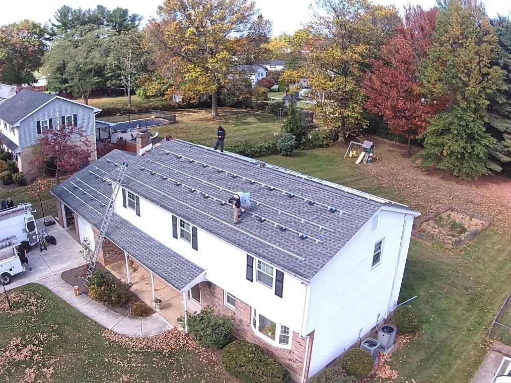 Workers on a two-story home roof, surrounded by fall foliage. 