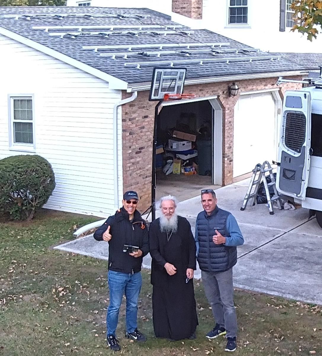 Three men giving thumbs up in front of a house with a basketball hoop over a garage.