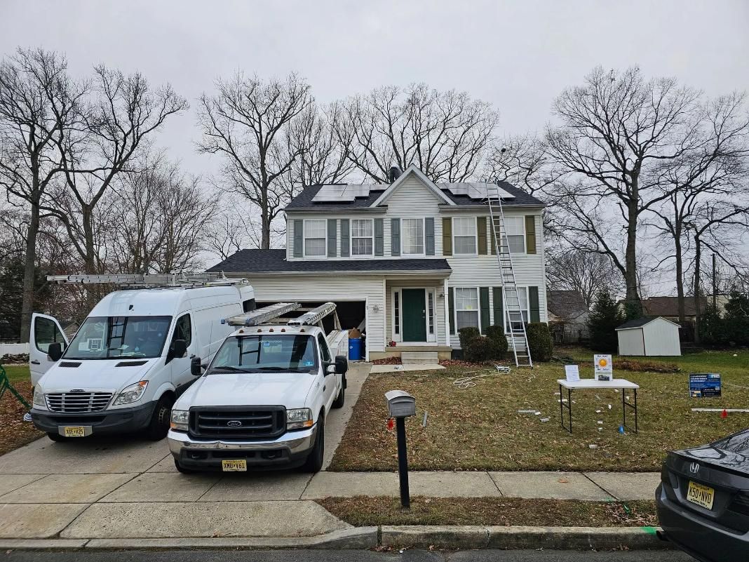 White house with solar panels being installed; service vehicles parked in the driveway.