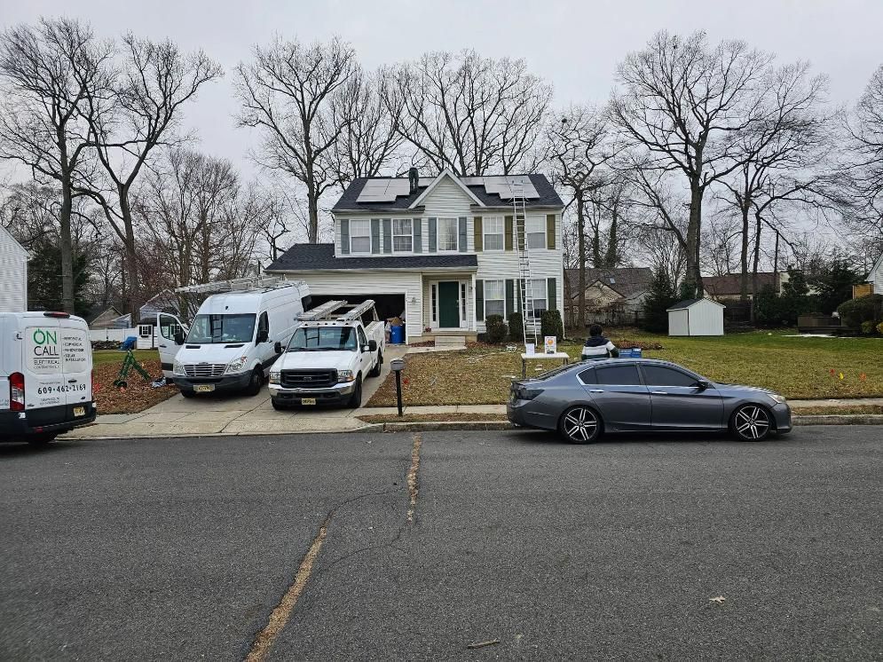 Two-story house with solar panels, parked work vans, a pickup truck, and a grey sedan on the street. 