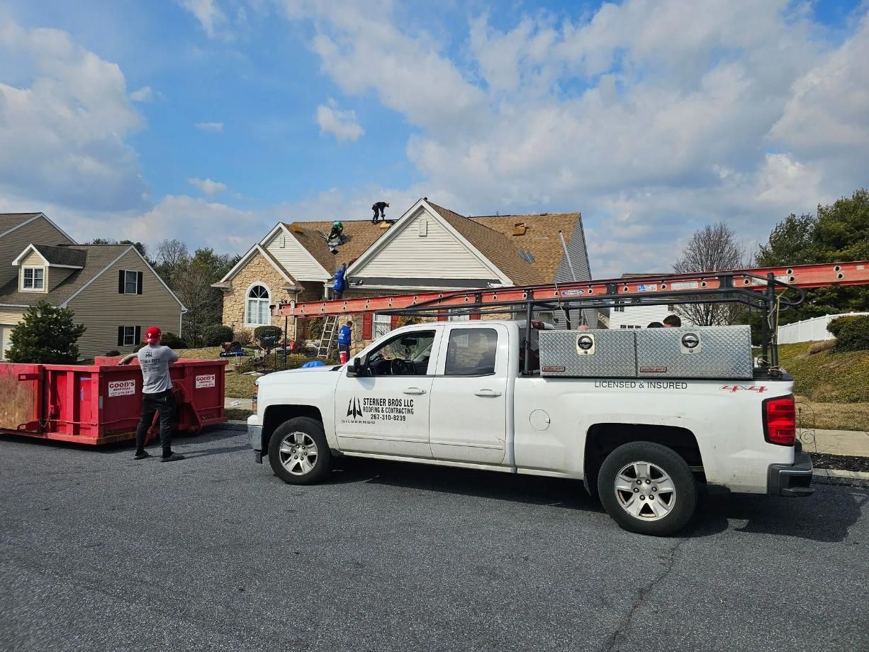 White truck with ladder rack parked on street in front of a house.
