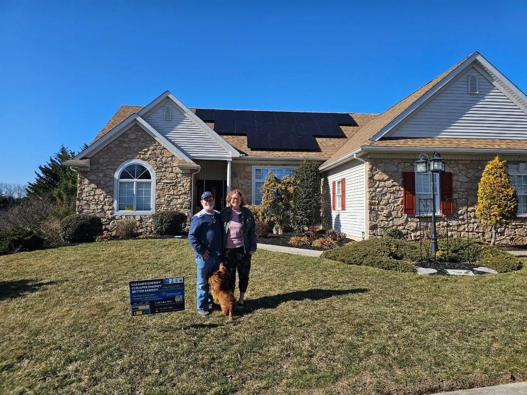 Couple and dog stand in front of a house with solar panels on the roof.