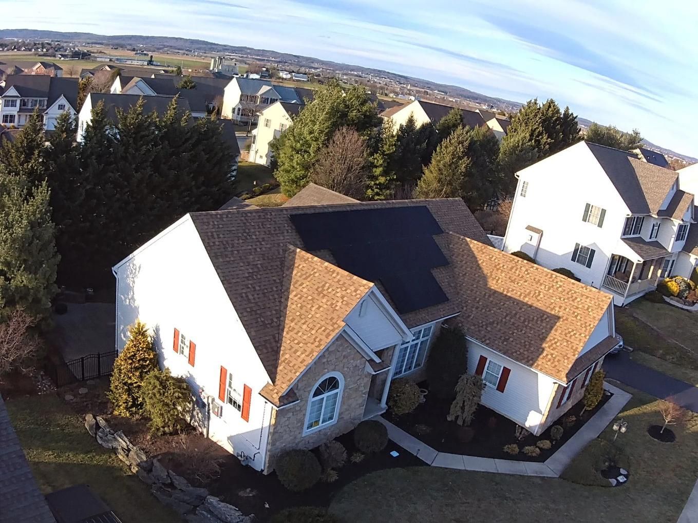 Aerial view of a house with solar panels on the roof, surrounded by other houses and trees on a sunny day.