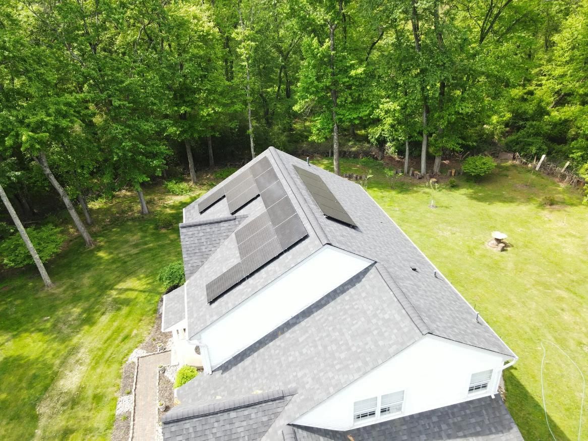 Solar panels installed on a house roof surrounded by green trees and grass.