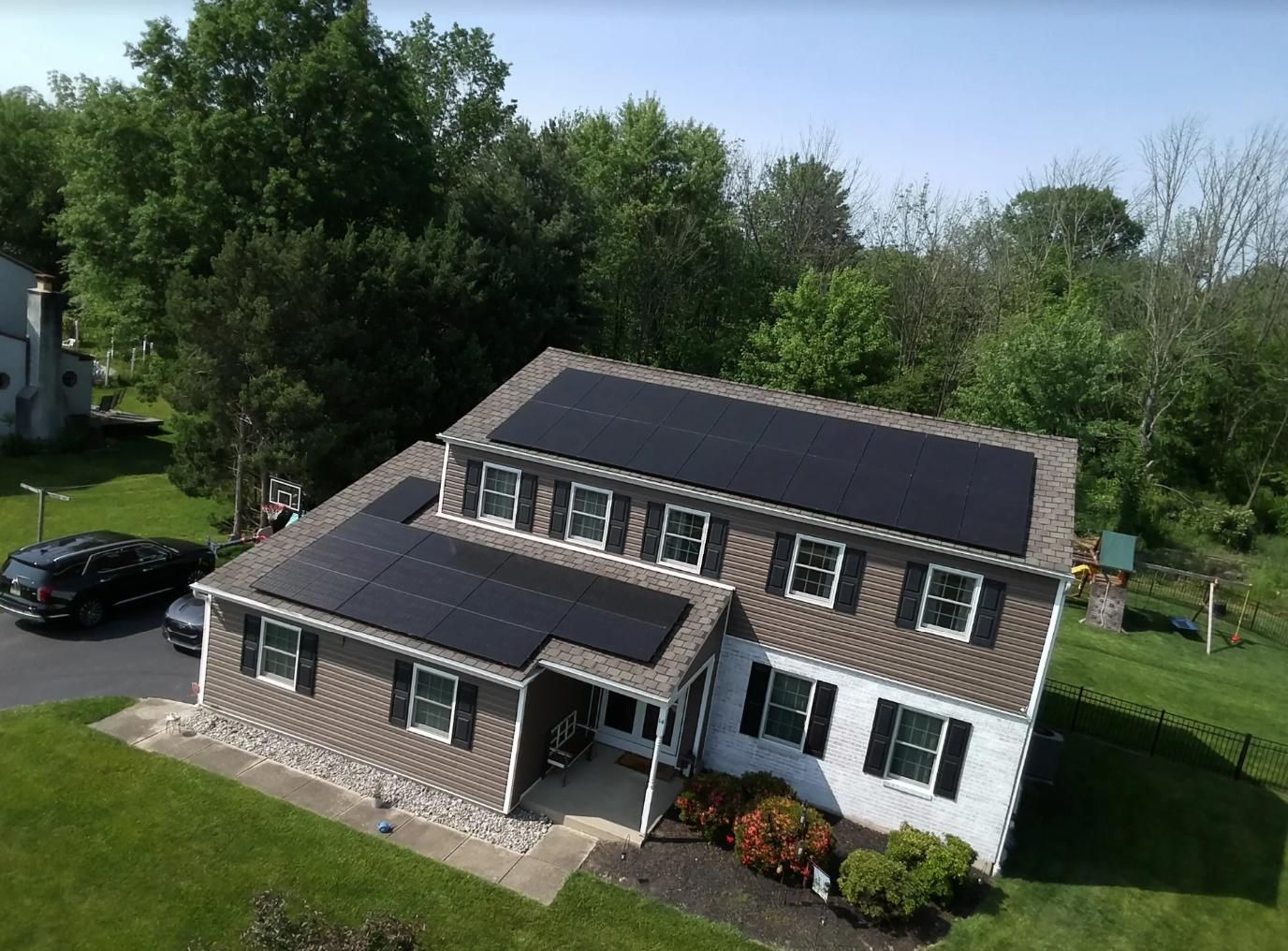 Solar panels on a house roof with green trees and a black car in the yard.