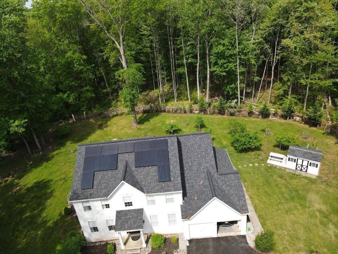 Aerial view of a white house with solar panels on the roof, surrounded by green grass and trees.