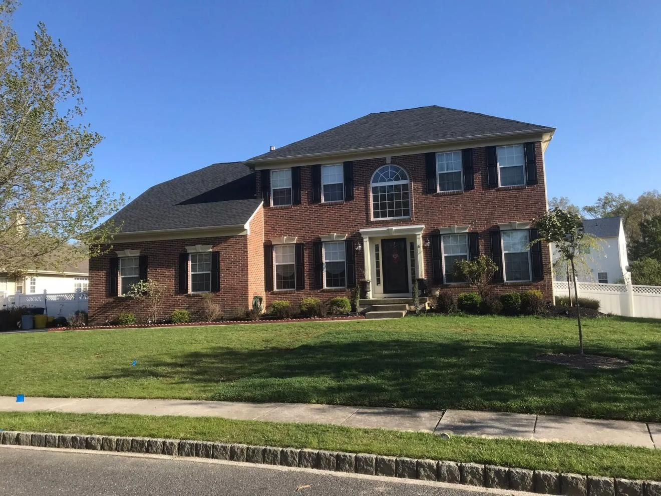 Two-story brick house with black shutters, green lawn, and blue sky.