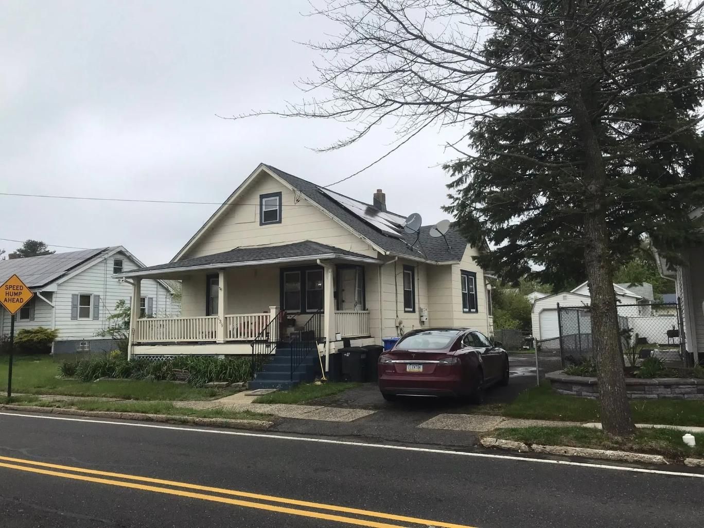 A two-story house with a porch and red car parked in front on a cloudy day.