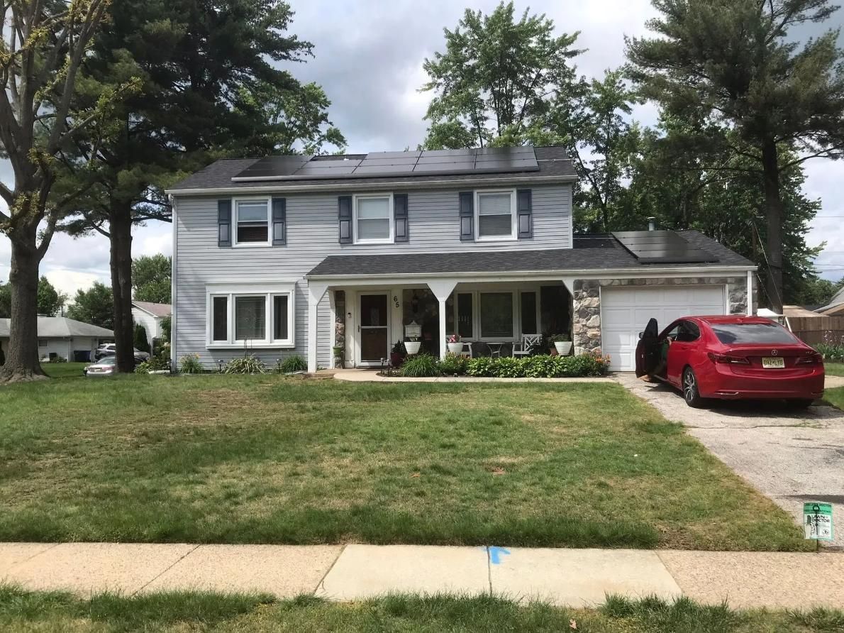 Two-story house with gray siding, solar panels, and a red car parked in the driveway. 