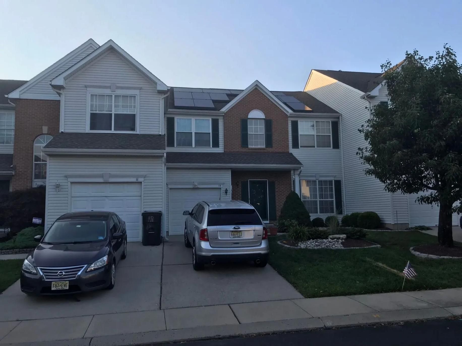 Two-story townhouse with parked cars in front. Solar panels on roof. 