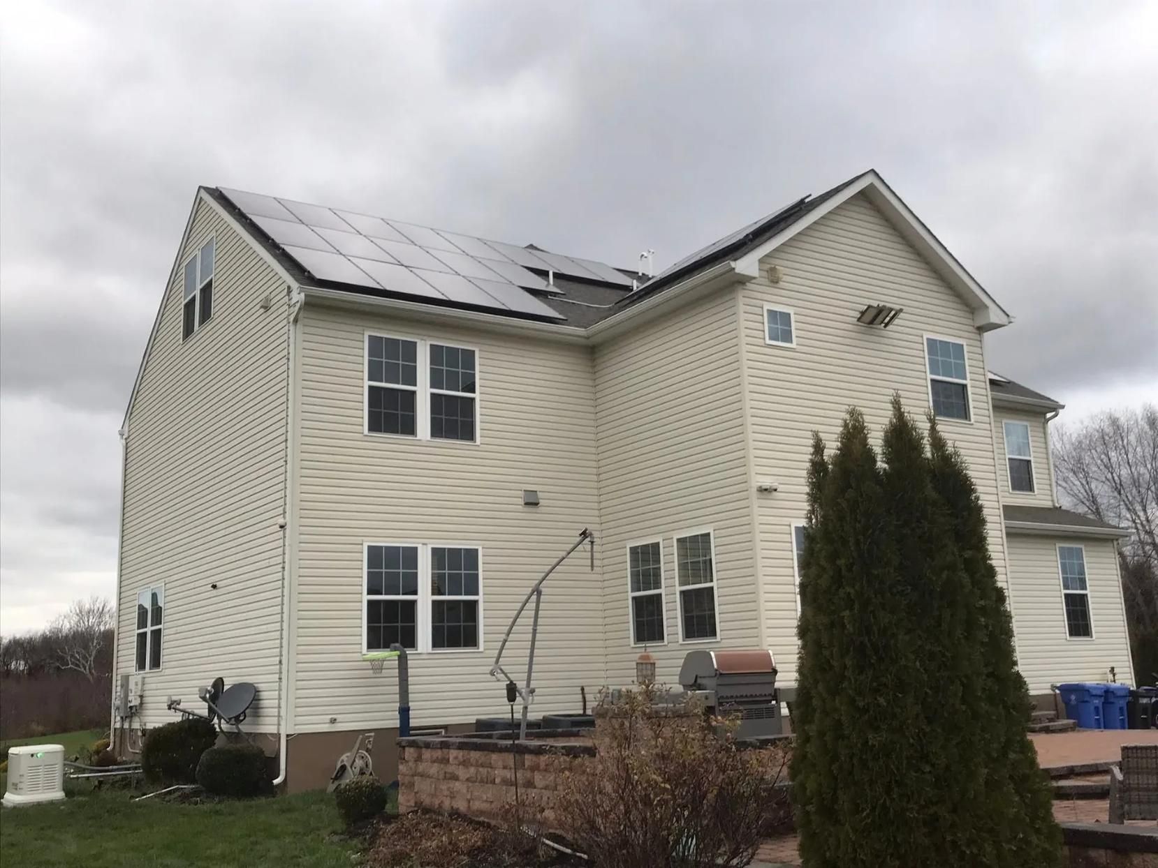 Beige house with solar panels on roof, under a cloudy sky.