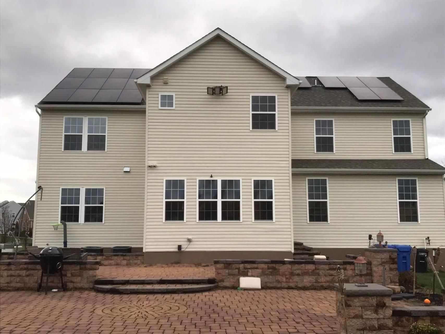 Back of a two-story beige house with solar panels on the roof and a brick patio.