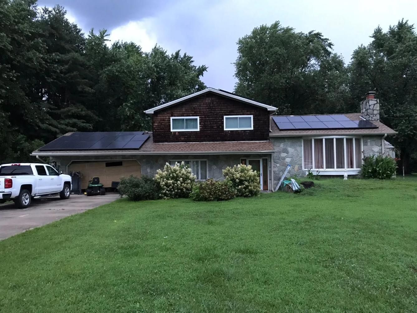 House with solar panels on roof, stone exterior, white pickup truck in the driveway, and green lawn.