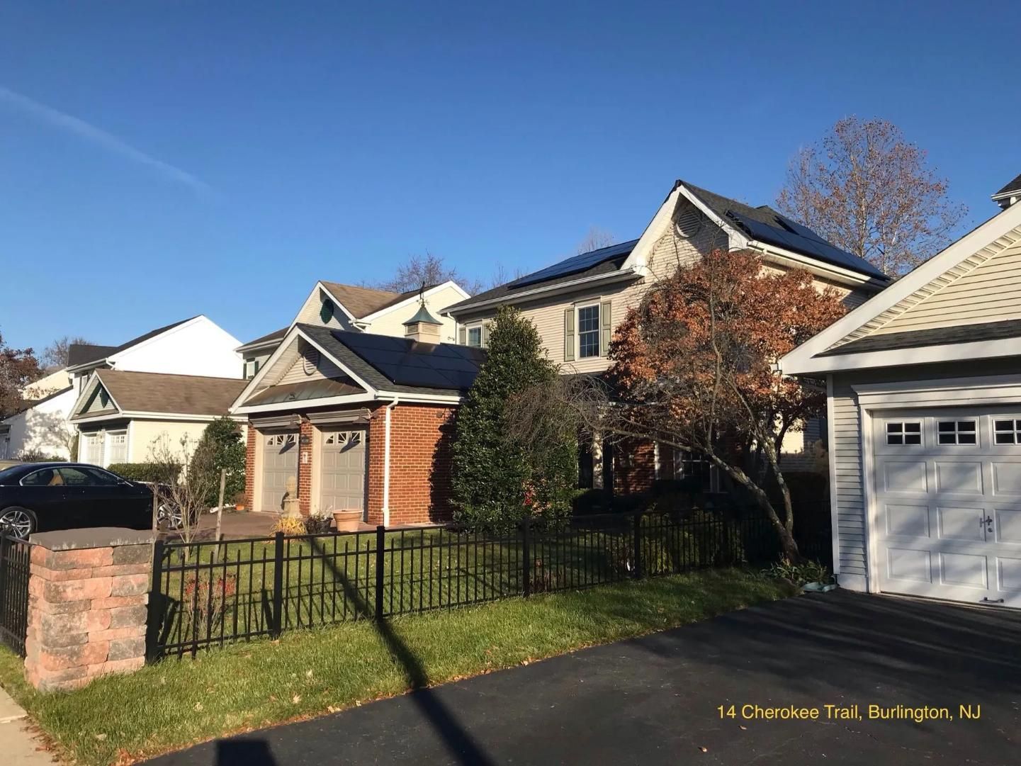 Houses with solar panels on roofs, brick and siding exterior, black fence, clear sky.
