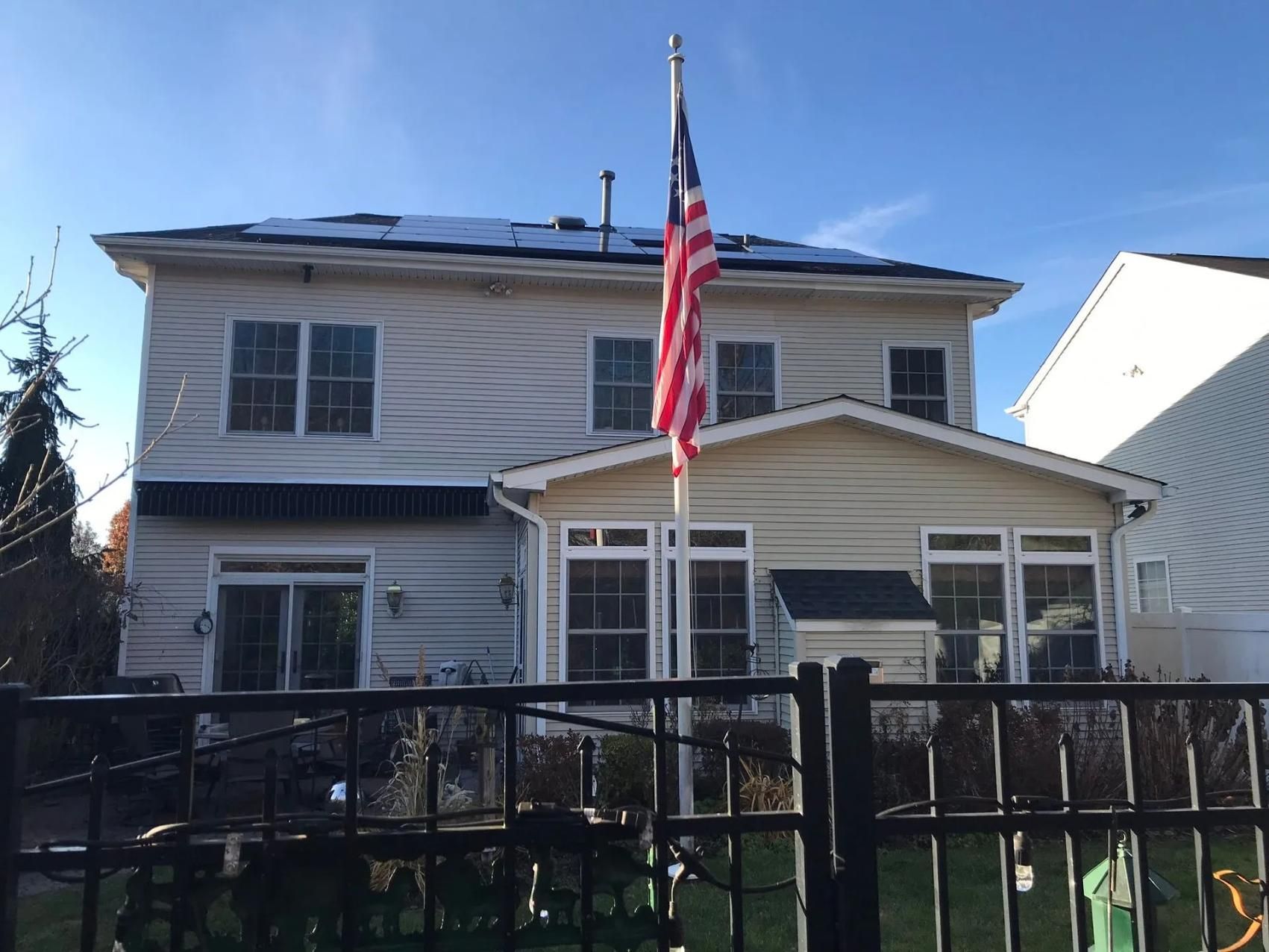 Two-story house with an American flag; the house has snow on the roof and is behind a black fence.