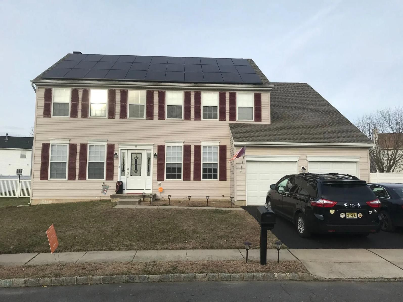 Two-story house with tan siding, burgundy shutters, solar panels, and a black SUV in the driveway.