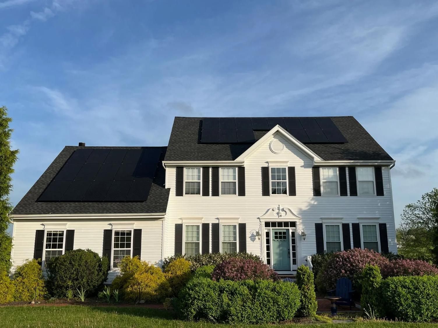 White house with black solar panels on the roof and black shutters. 