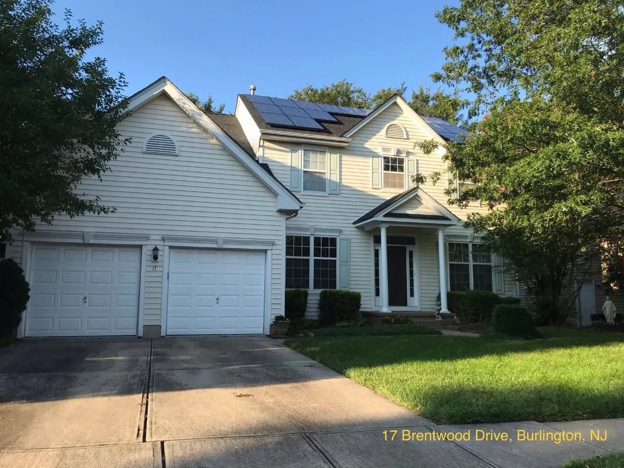 Two-story beige house with solar panels on the roof and a two-car garage. 