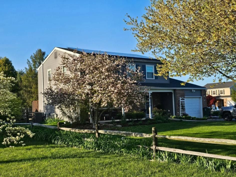 Two-story house with solar panels on roof, trees in front yard, sunny day.
