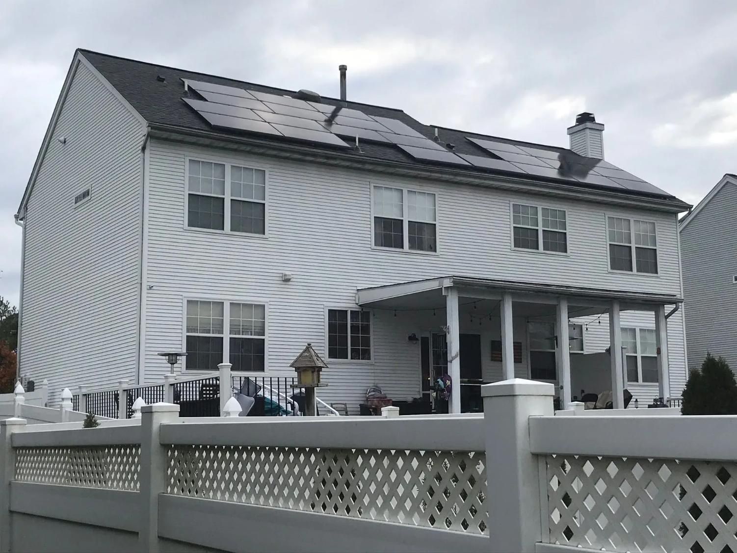 White house with solar panels on the roof and a white fence in the foreground. 
